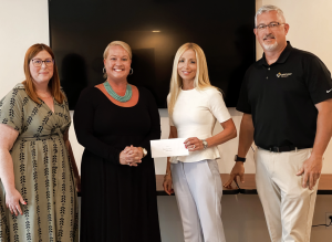 Three women and one man pose for a check presentation.